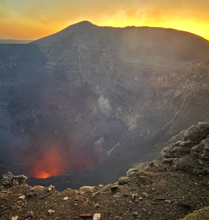 The silhouette of the Masaya Volcano crater rim against a dark orange dusk sky